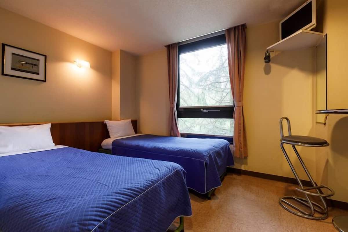 Habitació d'hotel amb dos llits, una finestra amb cortines, una taula petita i un televisor fixat a la paret.