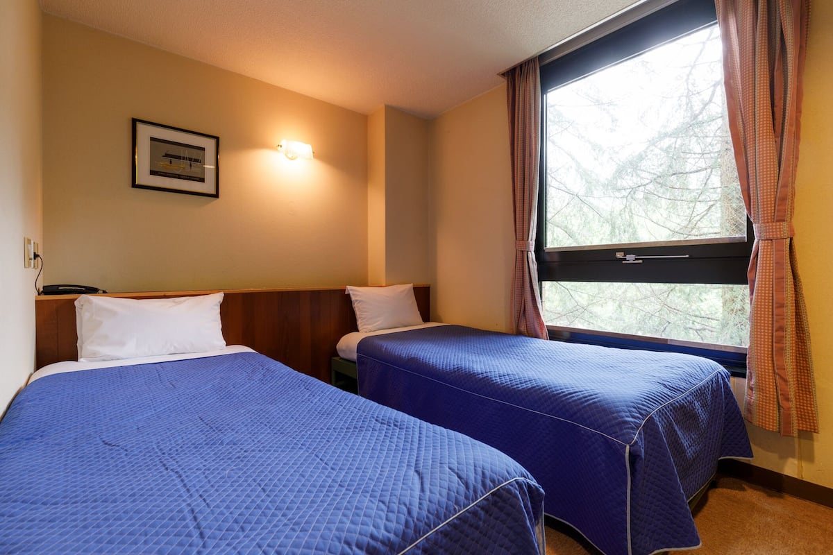 Habitació d'hotel amb dos llits, una finestra amb cortines, una làmpada de paret i un quadre amb marc.