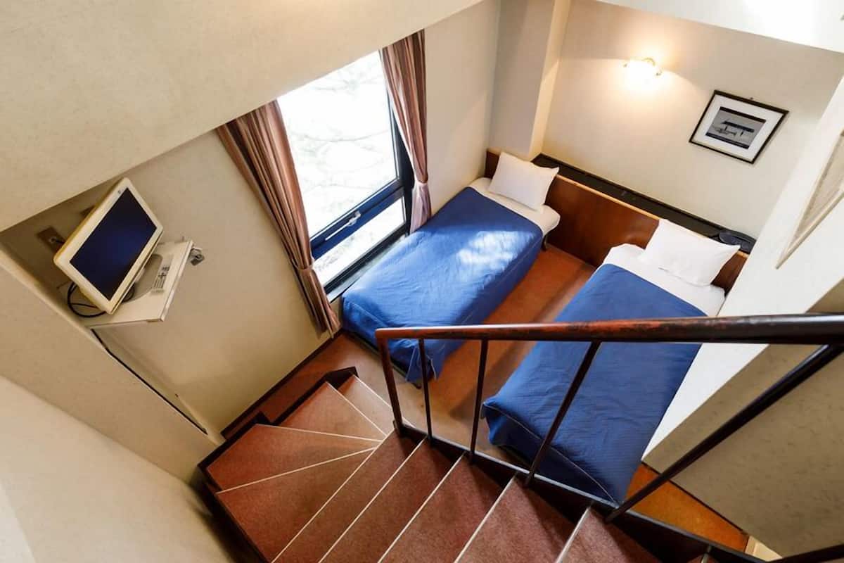 Habitació d'hotel amb dos llits, una finestra, escriptori amb ordinador i unes escales.