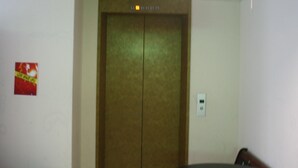Une porte d’ascenseur fermée dans une pièce où l’on aperçoit un interrupteur fixé au mur et une affiche accrochée au mur.