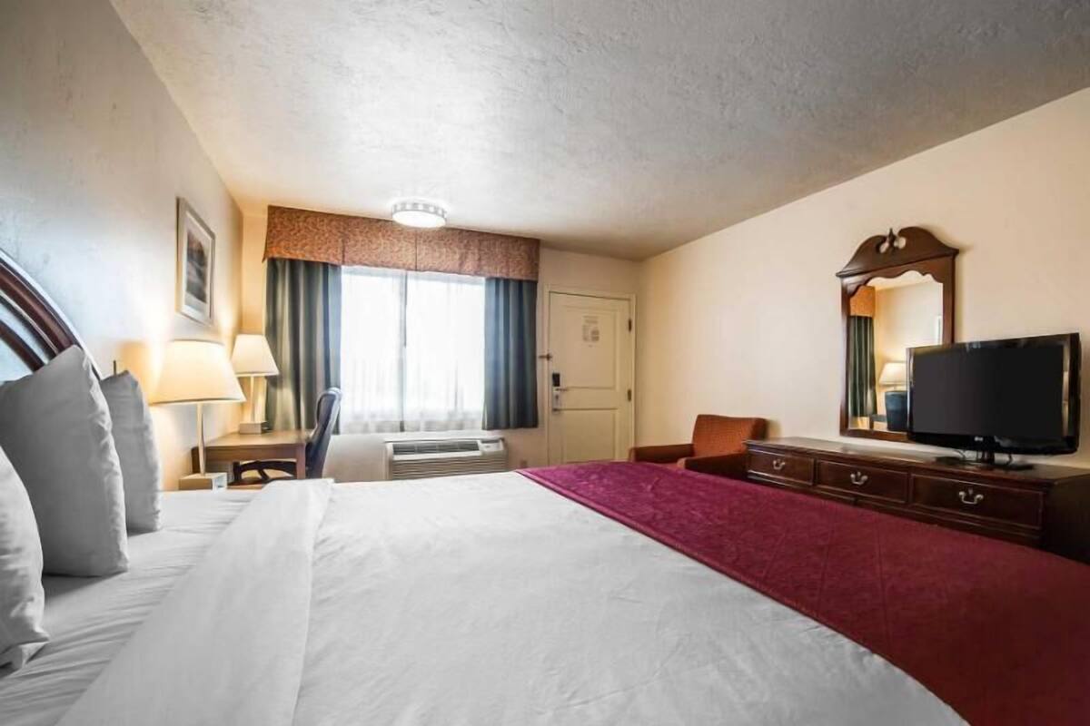 A hotel room with a large bed, a desk with a lamp, a television, and a window with curtains.