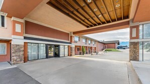 Ein Hotel mit Eingangsbereich, überdachtem Gang, Steinpfeilern und Parkplatz.
