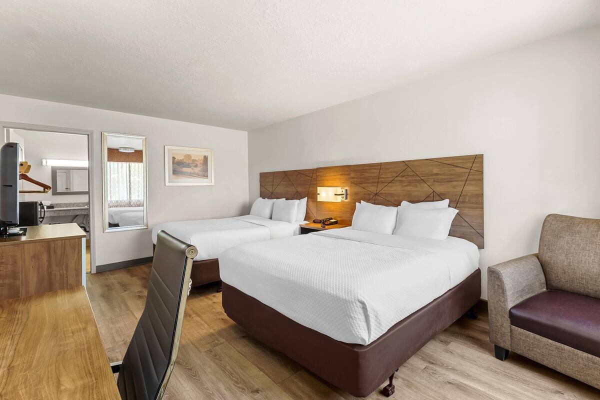 A hotel room with two beds, a desk, a chair, and a TV.