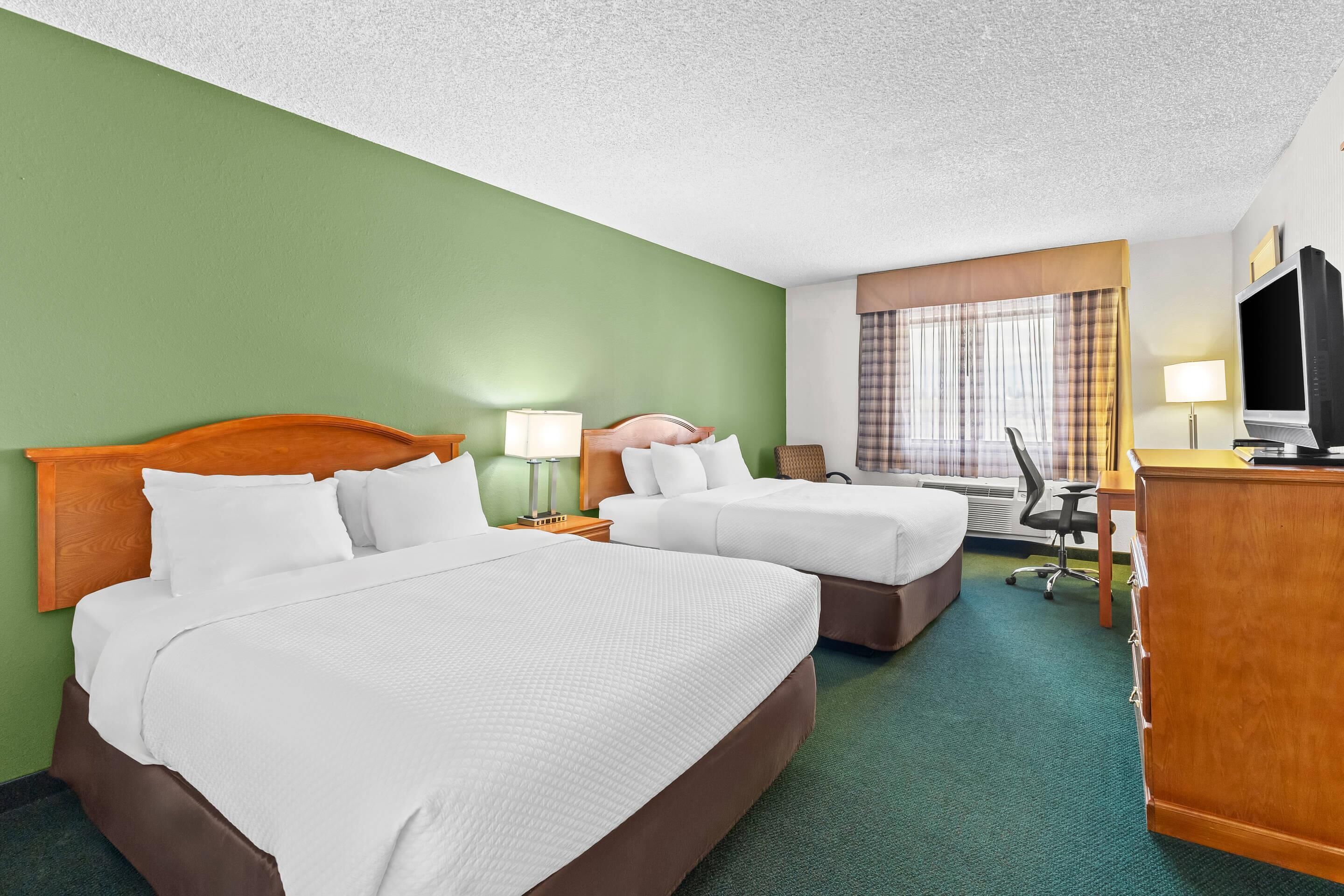 A hotel room with two beds, a desk, a television, and a window with curtains.