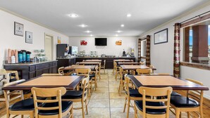 Ein Restaurant mit mehreren Tischen und Stühlen, einer Küchenzeile und einem an der Wand montierten Fernseher.