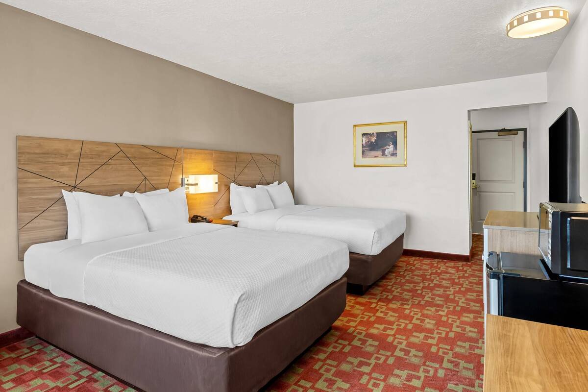 A hotel room with two beds, a wooden headboard, a wall-mounted TV, and a patterned carpet.
