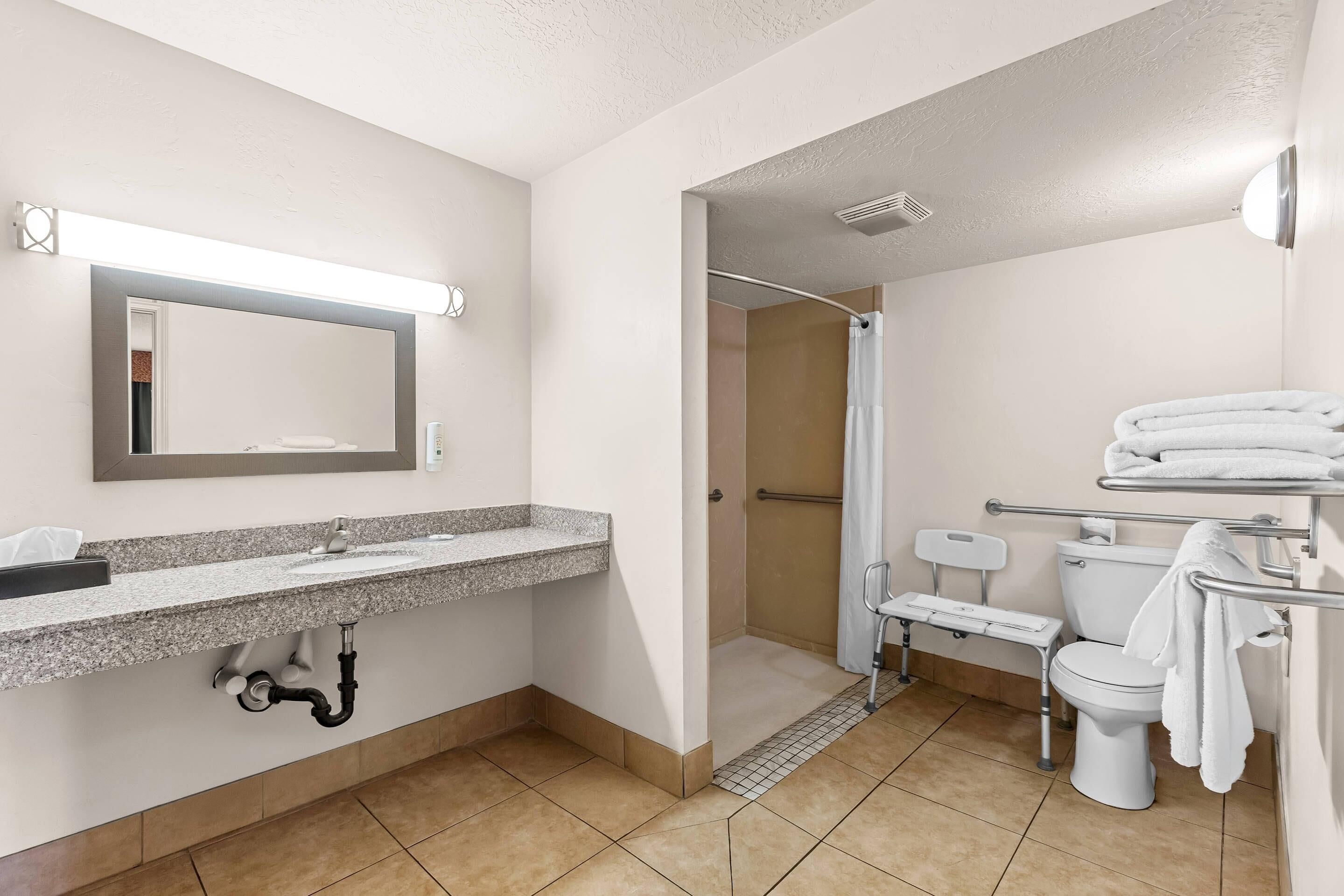 Ein modernes Badezimmer mit Marmorwaschtisch, Spiegel, Dusche mit Haltegriff, Toilette und Handtuchhalter.