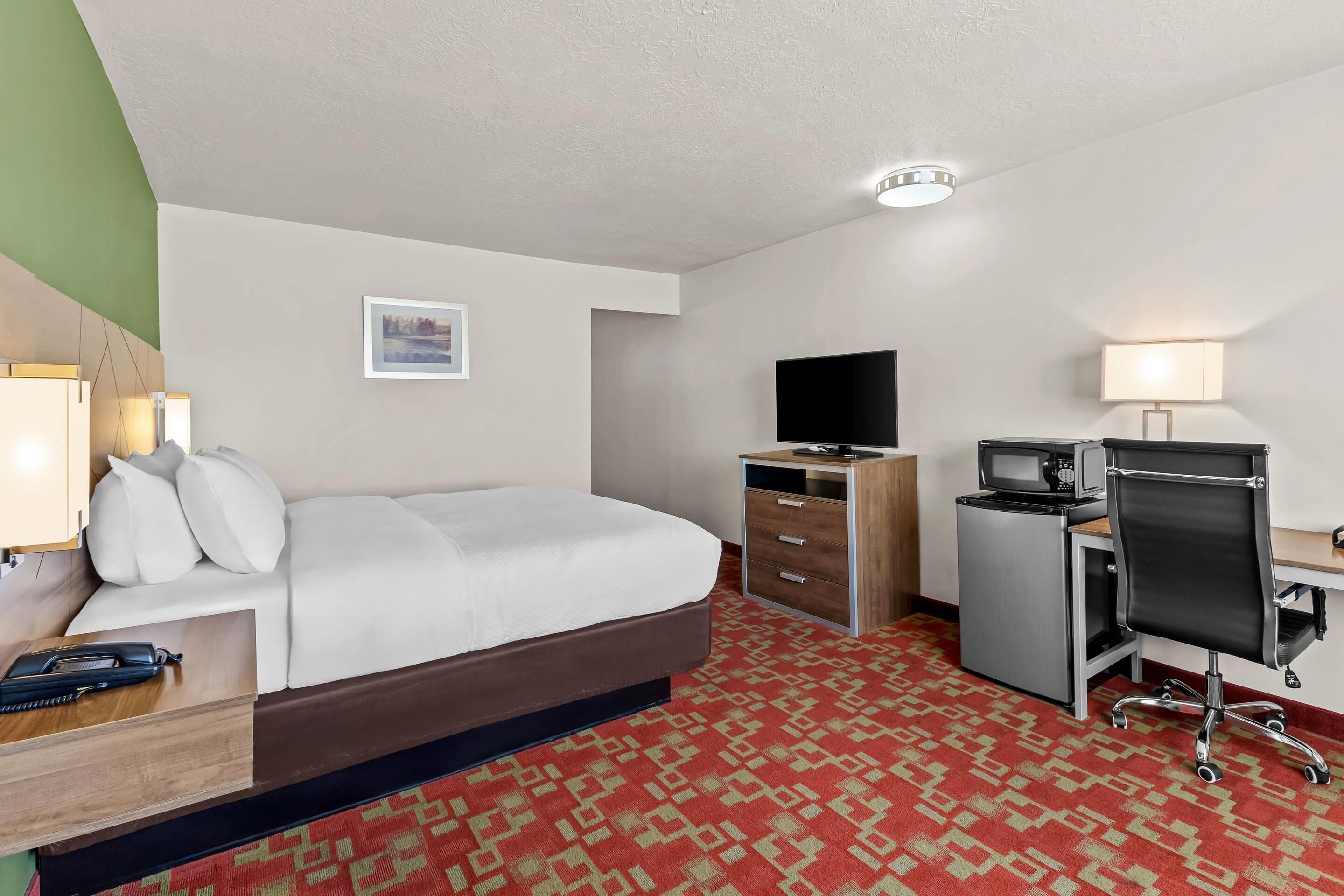 A hotel room with a bed, a desk with a computer, a television, and a lamp.
