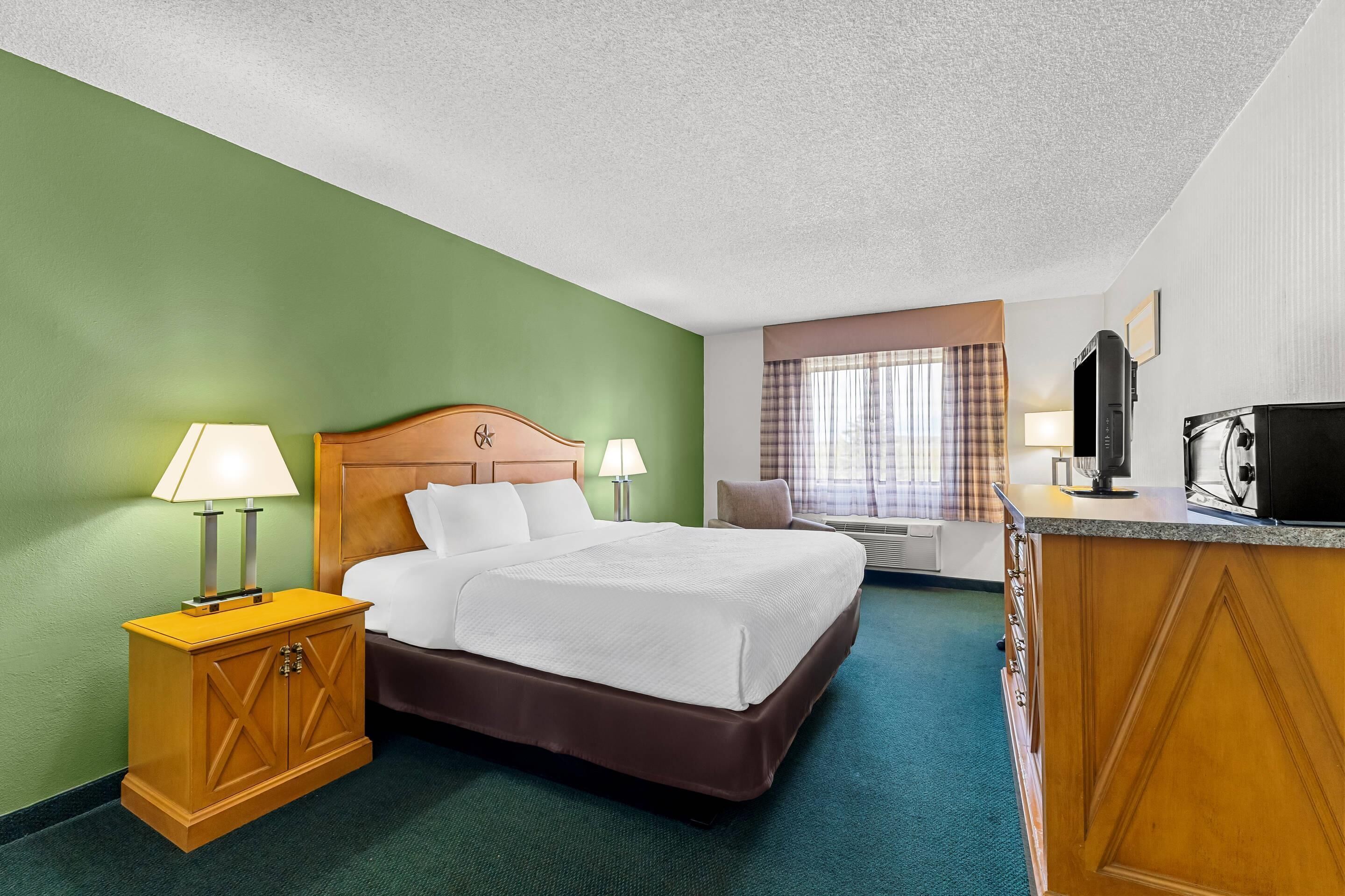A hotel room with a bed, bedside lamps, a desk with a television, and a window with curtains.