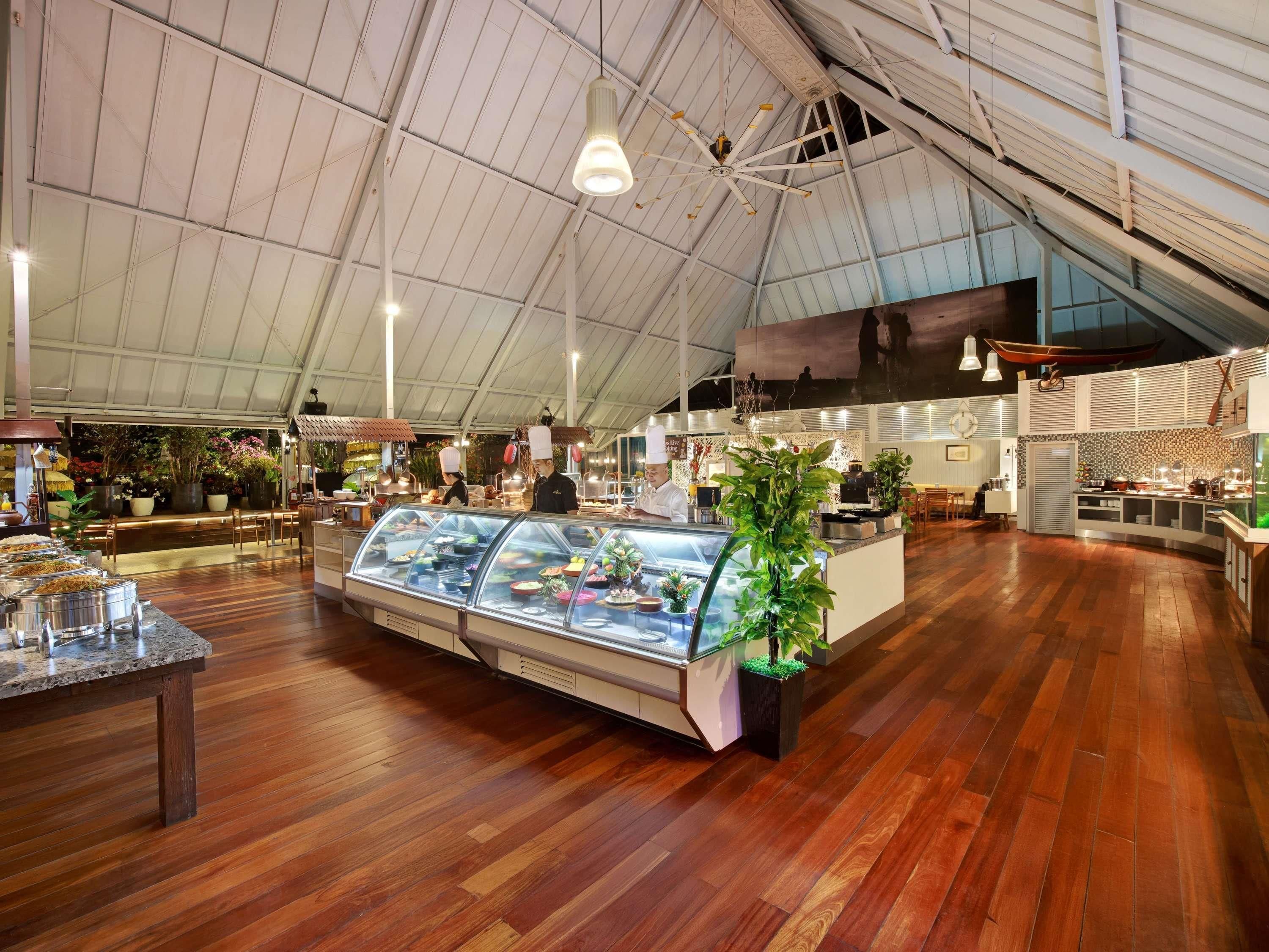 A spacious indoor area with a high ceiling, a central display case with food items, and a seating area with tables and chairs.