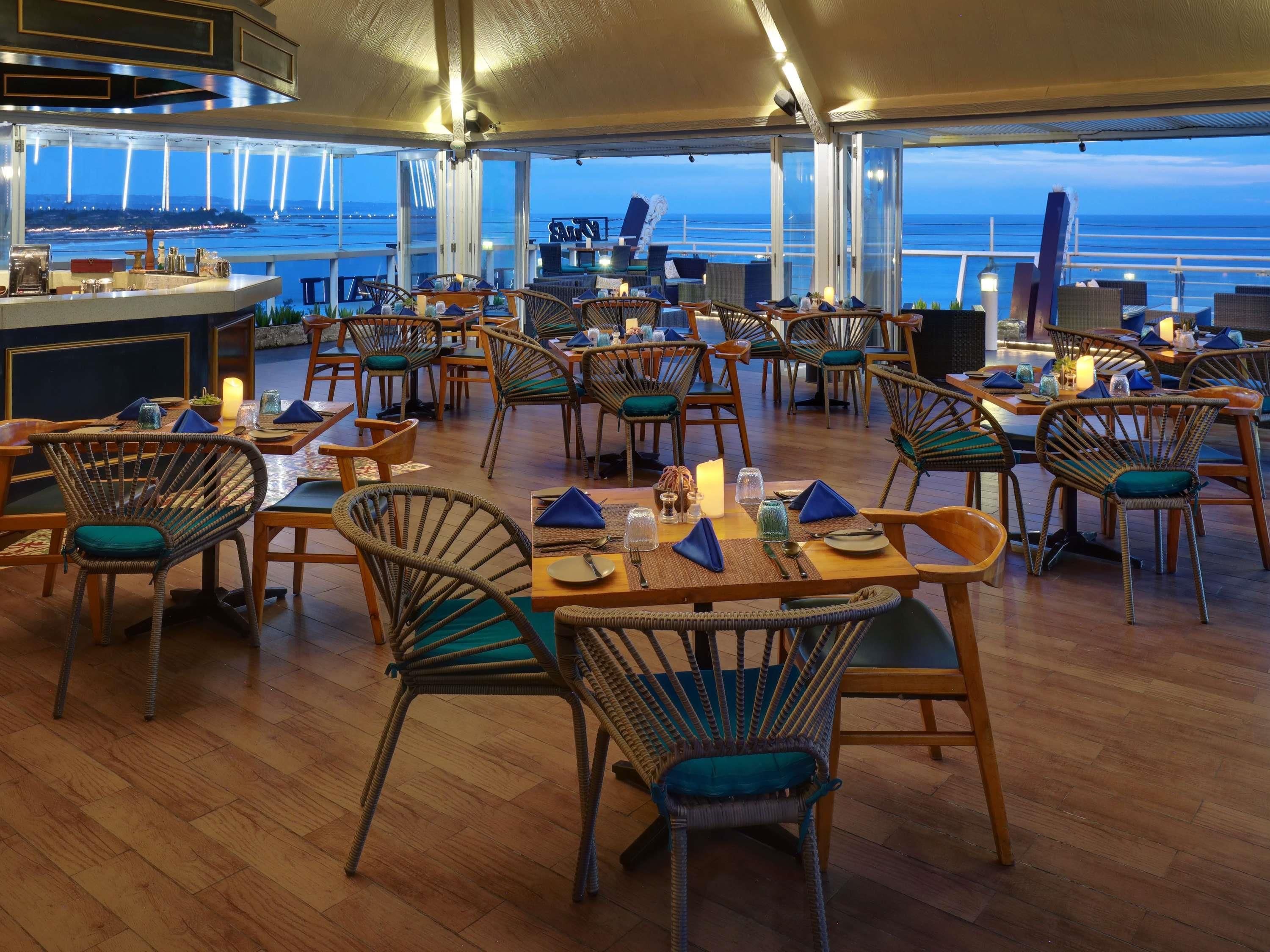 A restaurant with wicker chairs and tables, a bar area, and a view of the ocean.