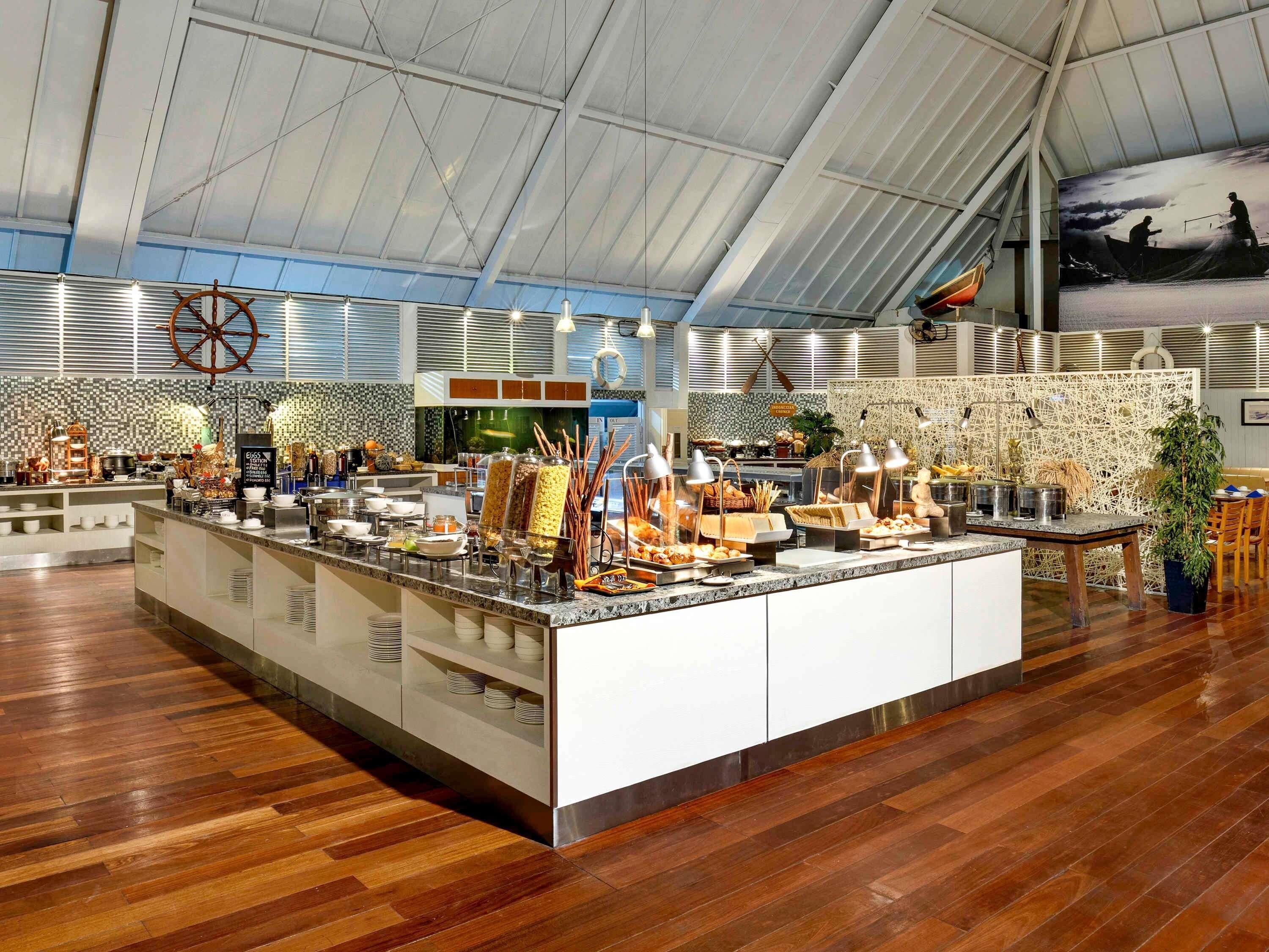 A spacious buffet area with a high ceiling and wooden flooring, featuring a variety of food items and a decorative wheel.