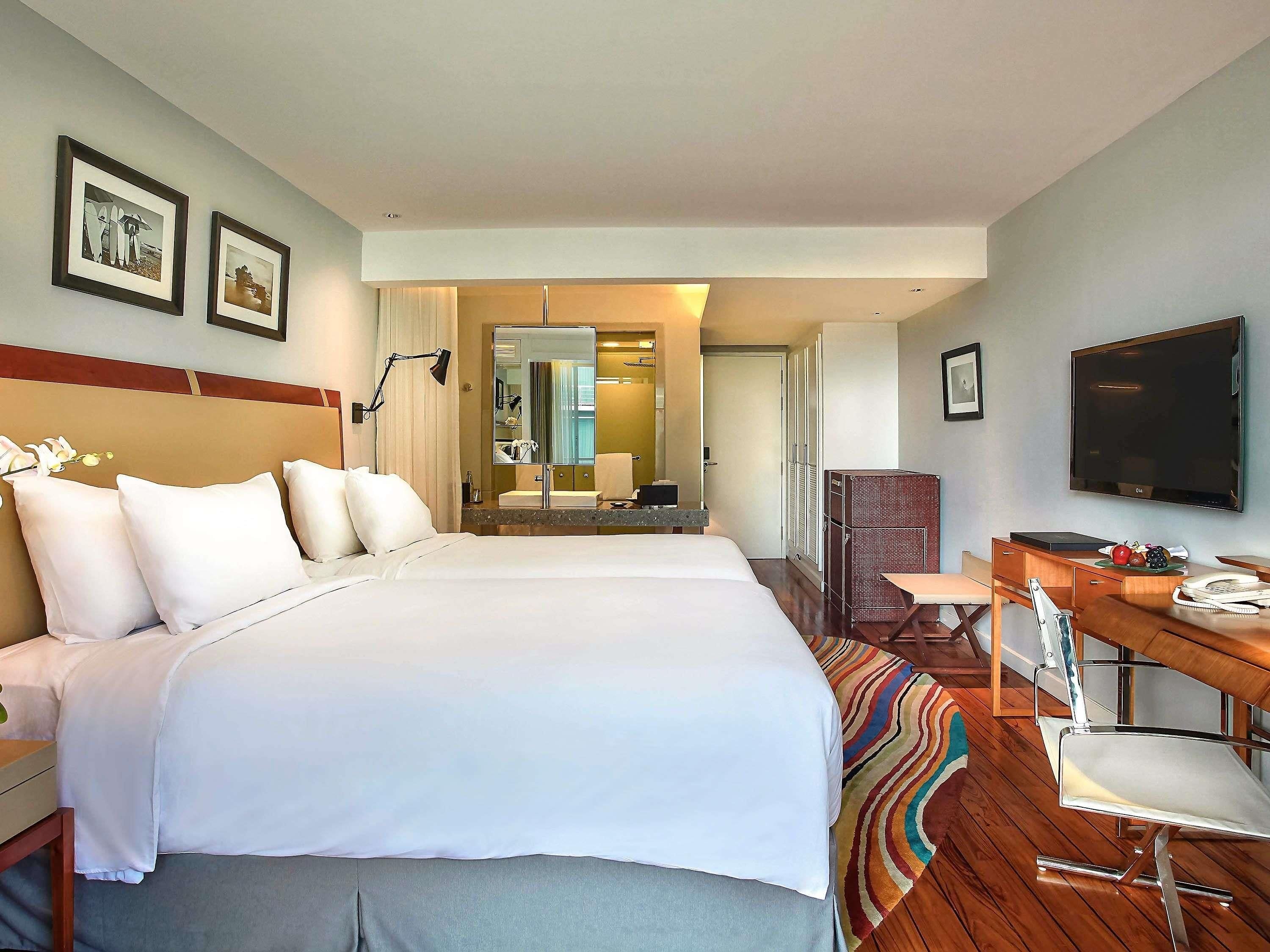 A hotel room with a large bed, a desk with a chair, a television, and a mirror.