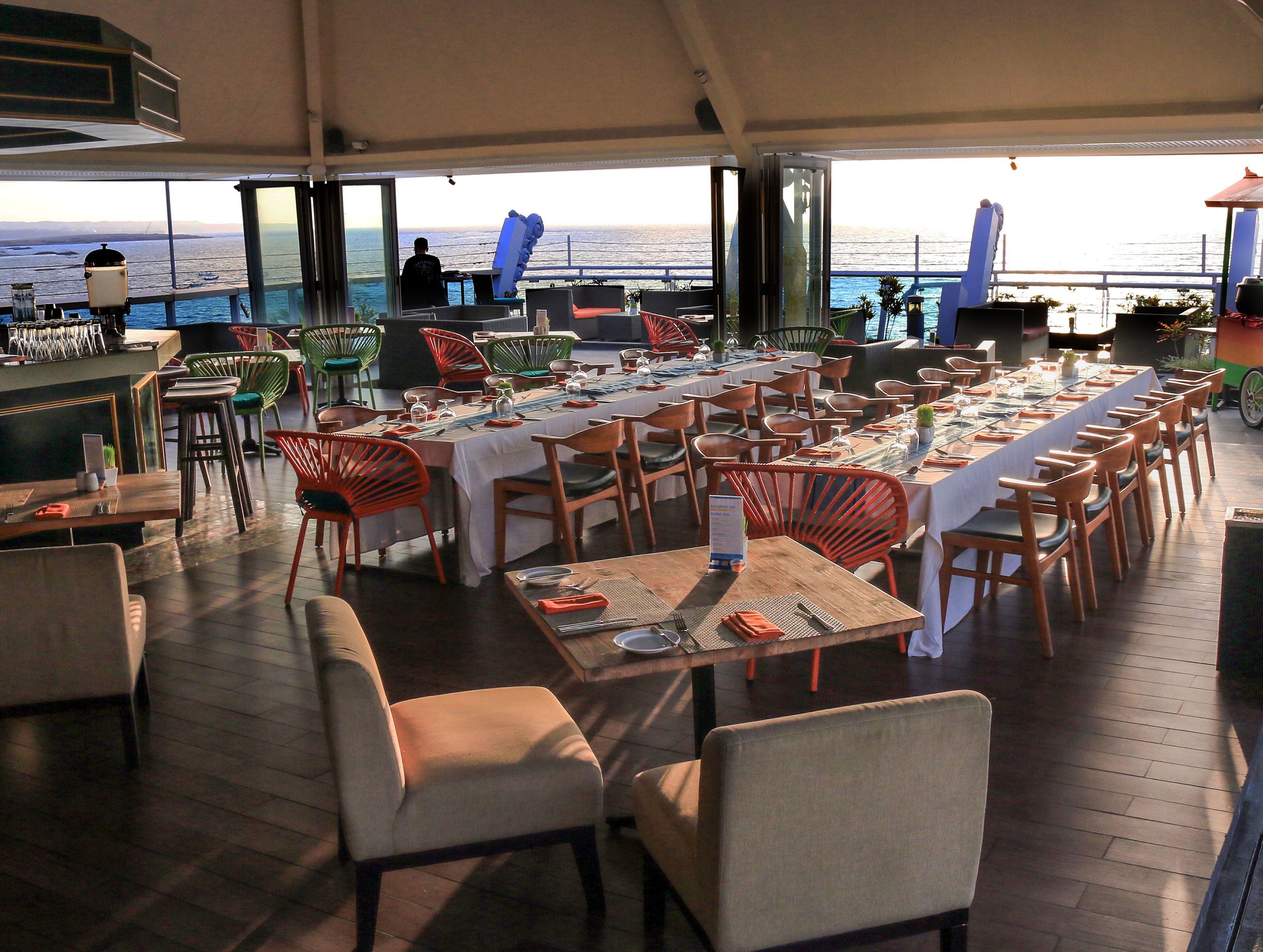 Comedor con mesas dispuestas para varios comensales, sillas y vista al océano.