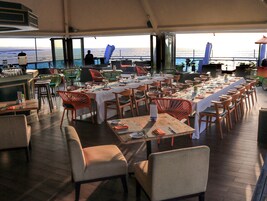 A dining area with tables set for multiple guests, chairs, and a view of the ocean.