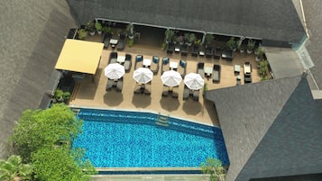 Vista aérea de una zona de piscina hotelera con tumbonas y sombrillas, rodeada de vegetación y arquitectura moderna.