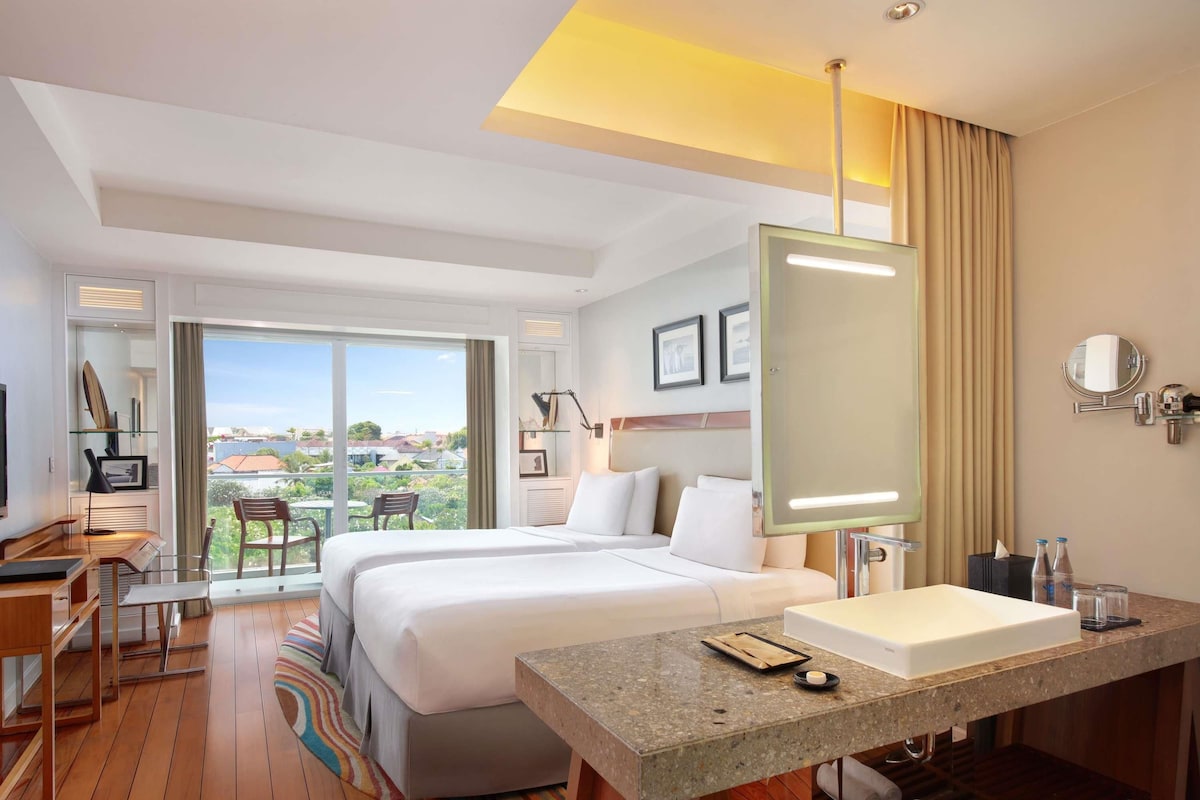 Ein Hotelzimmer mit einem großen Bett, einem Schreibtisch, einem Badezimmer mit Waschbecken und Blick auf die Stadt.