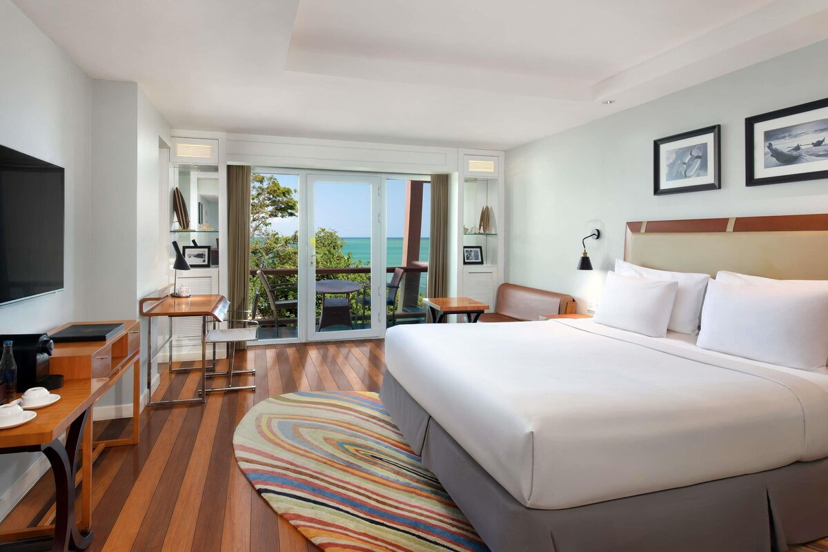 Ein Hotelzimmer mit Bett, Schreibtisch, Stuhl, Fernseher und Meerblick.