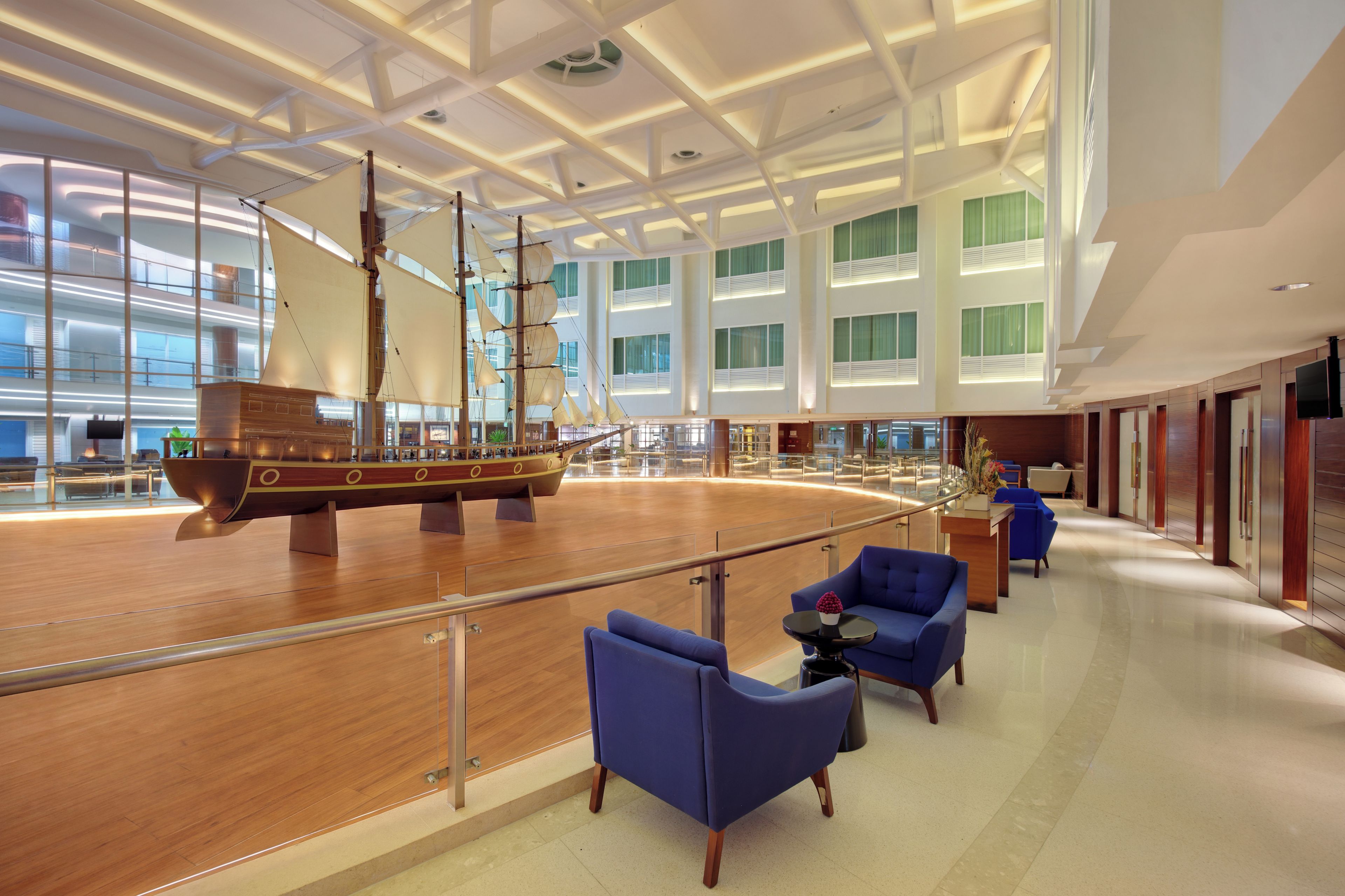 Un vestíbulo amplio con un gran modelo de barco de madera, asientos modernos y un alto techo con tragaluces.