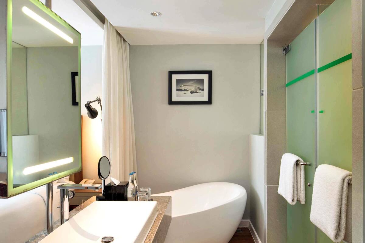 Uma casa de banho moderna com uma banheira independente, um espelho grande, um quadro emoldurado na parede e uma área de chuveiro com divisória de vidro.