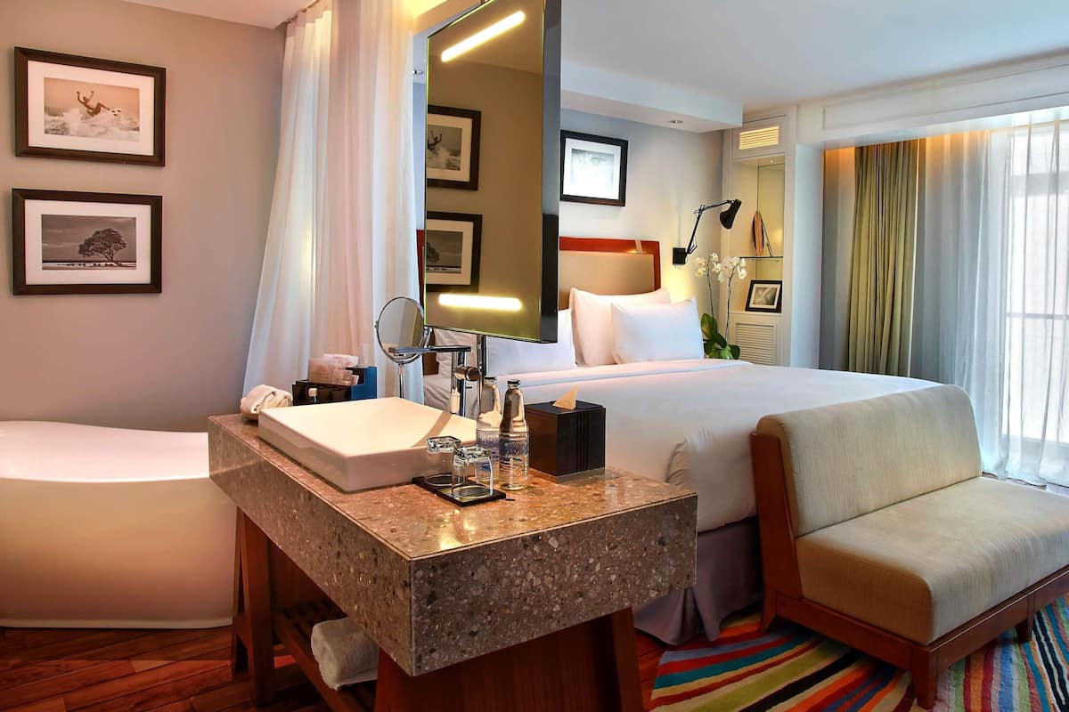 Quarto de hotel com cama, área de estar, banheiro com pia e espelho.