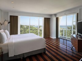 A hotel room with a large bed, a TV, and a view of the ocean.