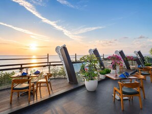 A terrace with tables and chairs, overlooking a sunset over the sea.