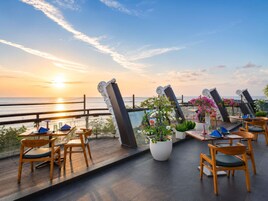 A terrace with tables and chairs, overlooking a sunset over the sea.