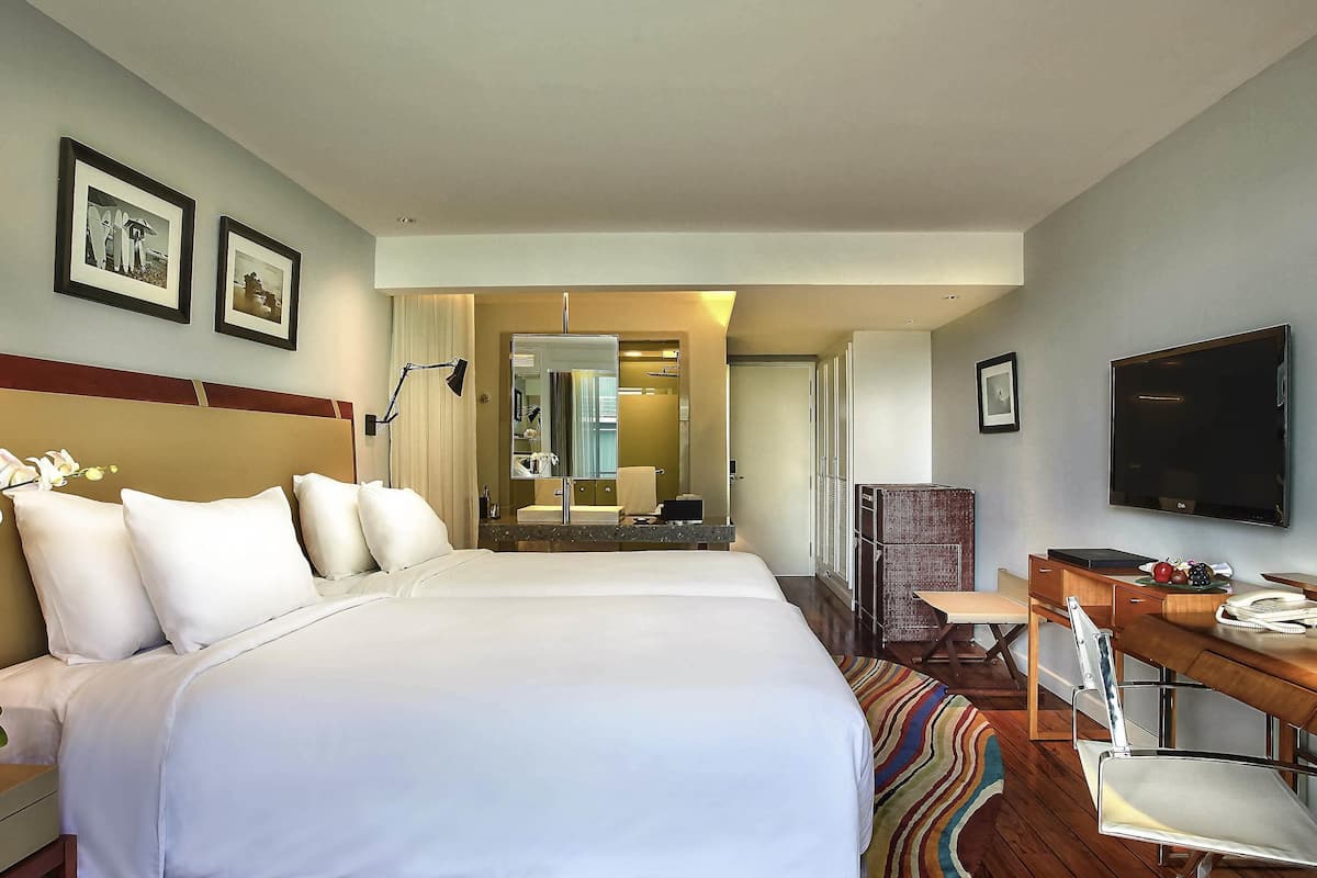 A hotel room with a large bed, a desk with a chair, a television, and a bathroom visible through an open door.