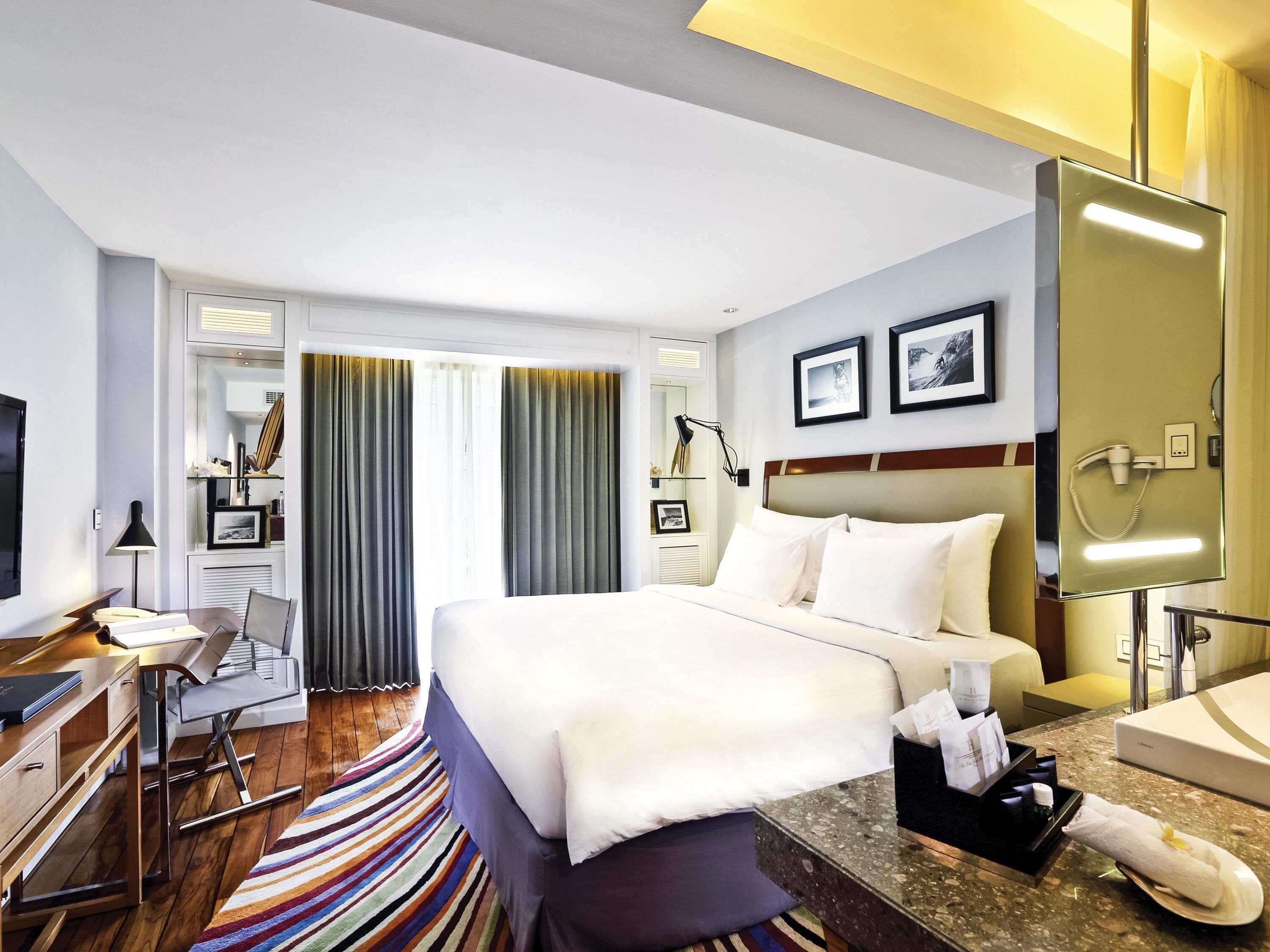 A hotel room with a bed, desk, chair, and a bathroom with a sink and mirror.
