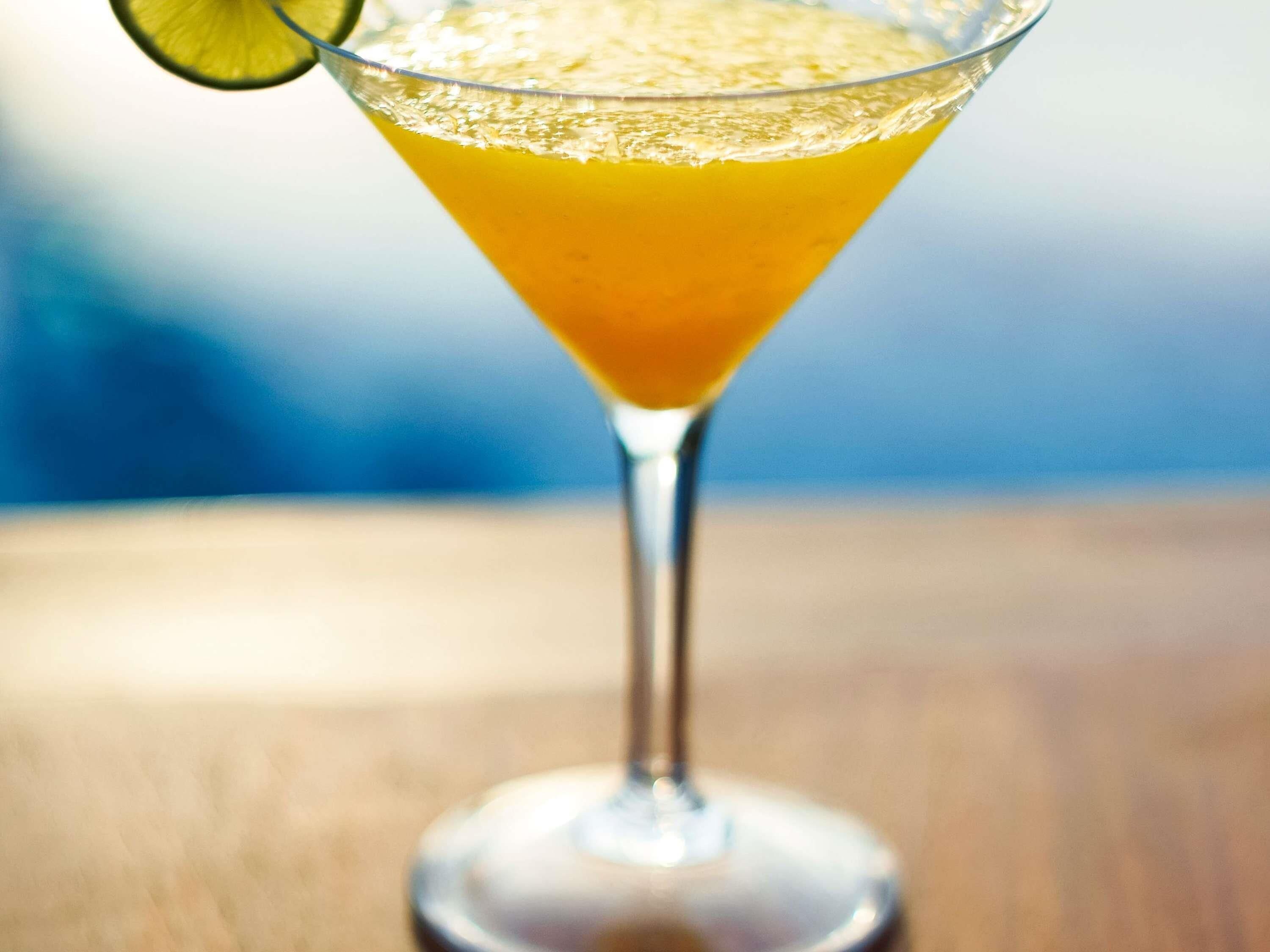 A cocktail in a martini glass with a lime garnish on the rim.