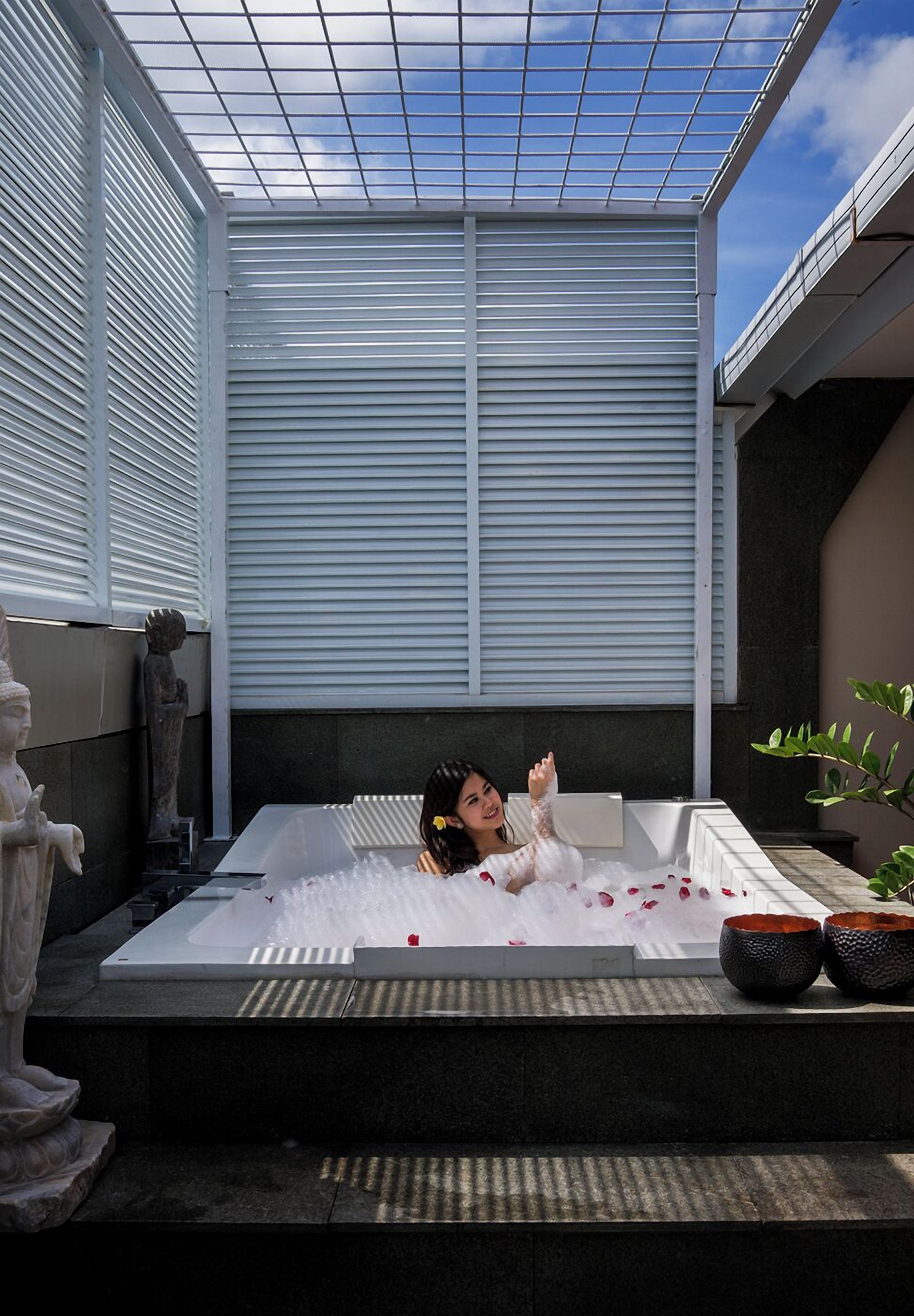 Una persona relajándose en un amplio jacuzzi blanco, con pétalos de rosa esparcidos.
