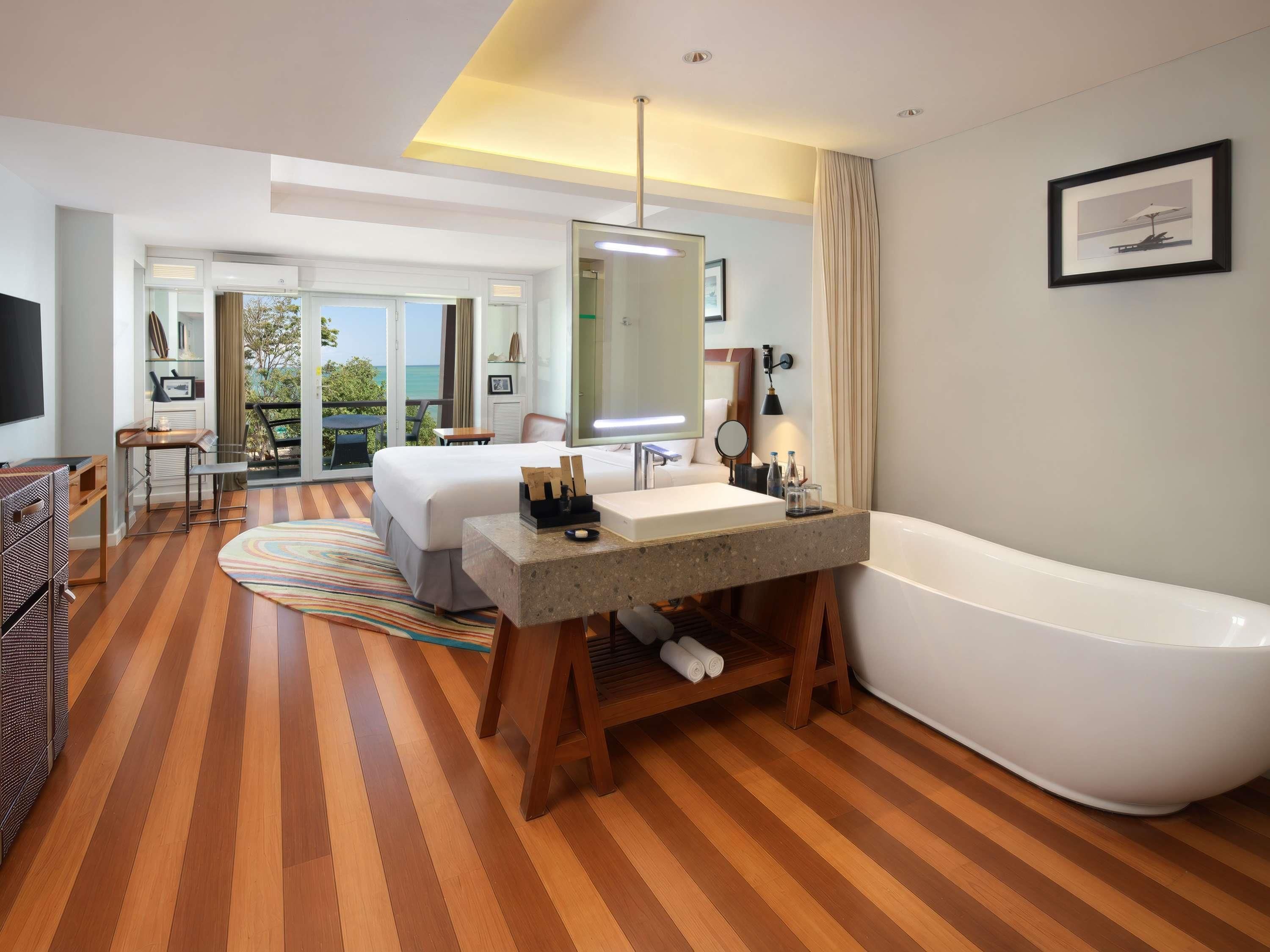 Habitación de hotel con una cama grande, una bañera, un tocador con espejo y un escritorio con silla.
