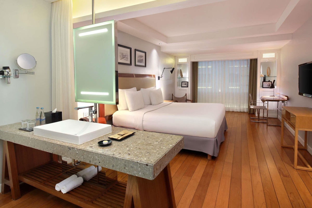 Ein Hotelzimmer mit Bett, Schreibtisch, Stuhl, Fernseher, Spiegel und einem Badezimmer mit Waschbecken und Toilette.