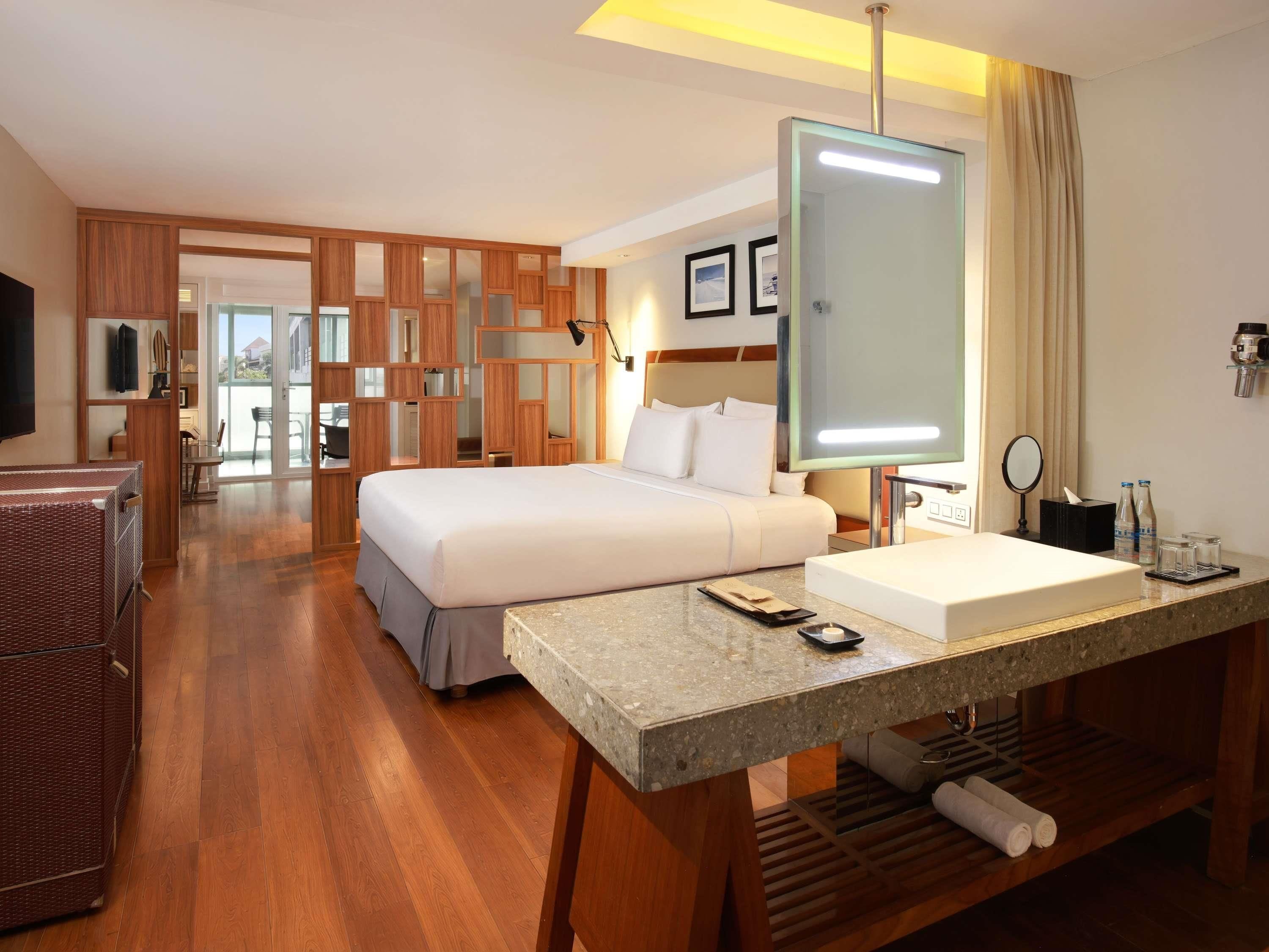 A hotel room with a bed, a desk with a sink, a television, and a bathroom visible through an open door.