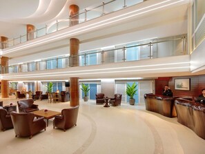 Un hall d’entrée spacieux, doté de sièges en cuir, d’un comptoir de réception et d’un plafond haut orné de rampes en verre.