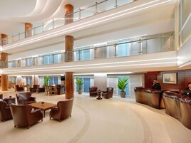 A spacious lobby with leather seating, a reception desk, and a high ceiling with glass railings.