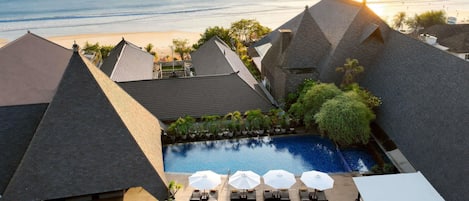 A rooftop pool area with lounge chairs and umbrellas, overlooking a beach and ocean.