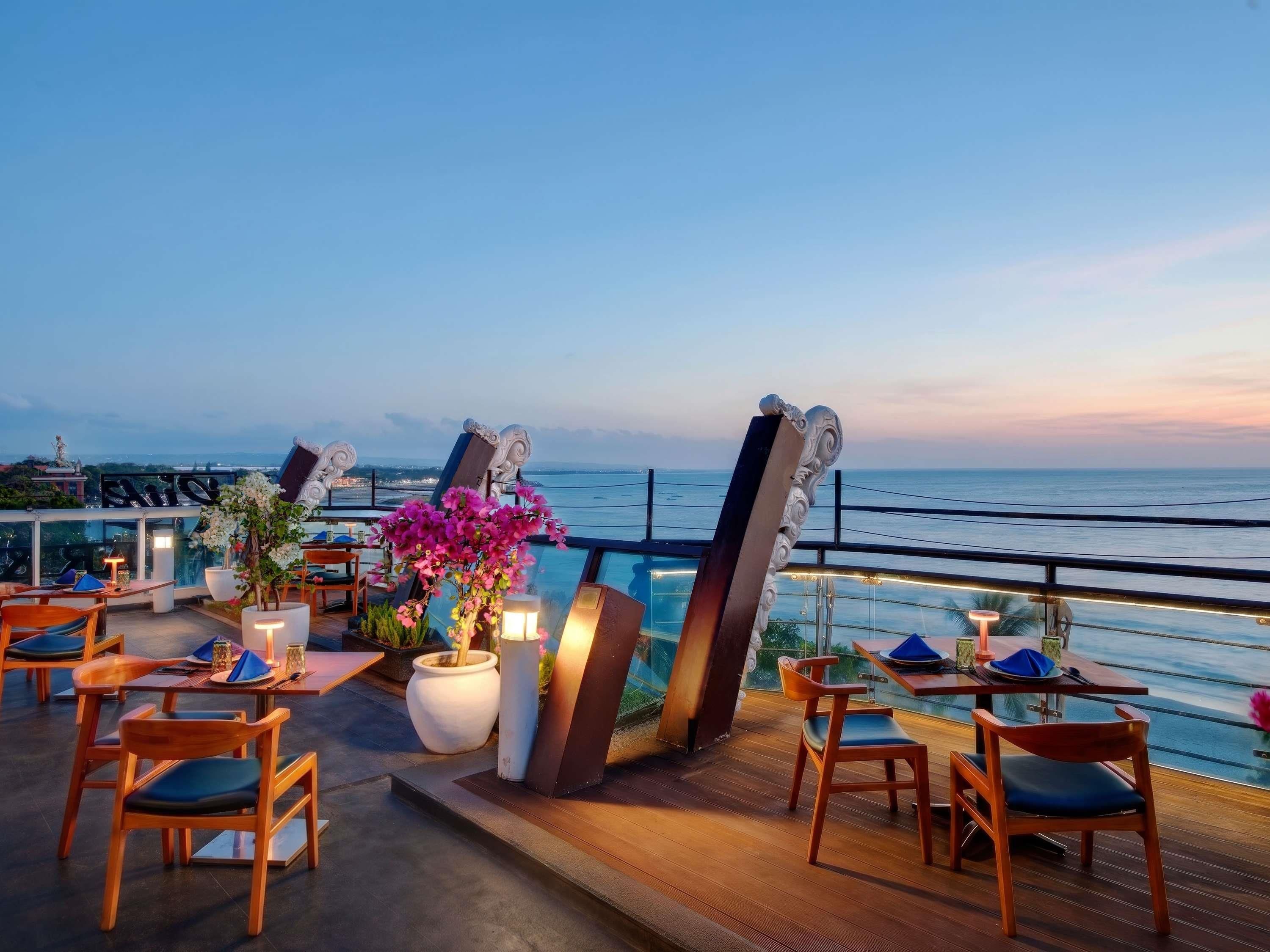 A rooftop terrace with tables and chairs, overlooking a body of water.