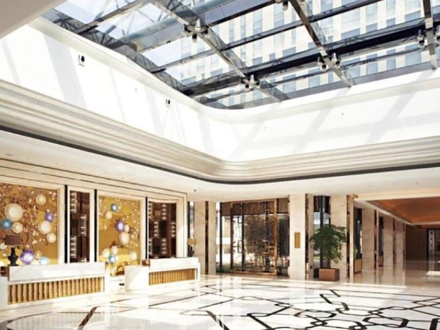 A spacious lobby with a high ceiling and a glass atrium, featuring a reception desk and seating area.