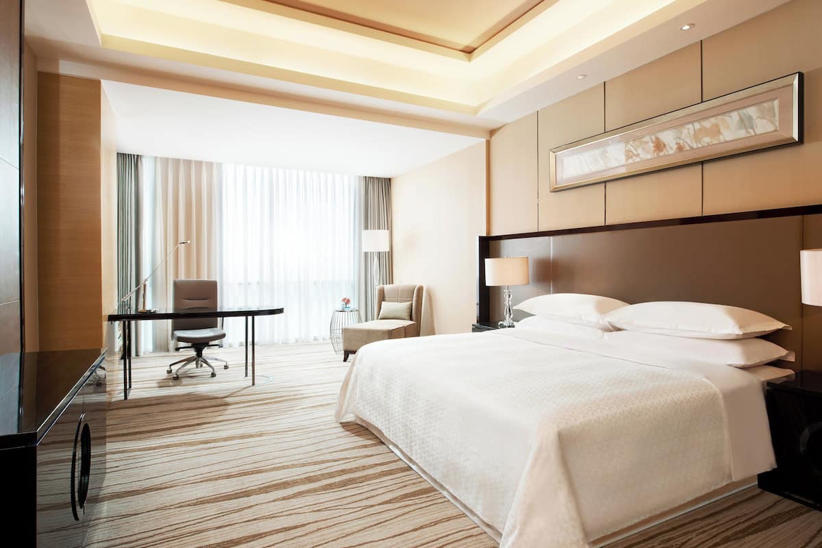 A hotel room with a large bed, a desk, a chair, and a window with curtains.