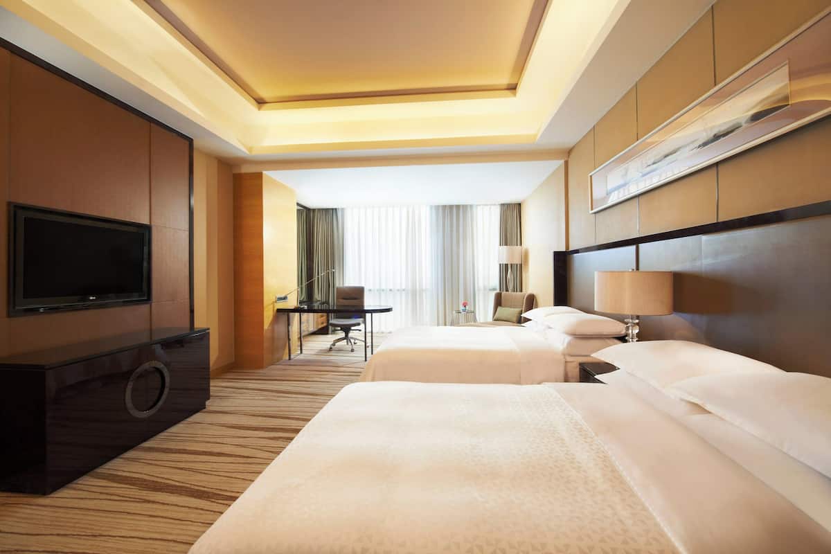 A hotel room with two beds, a TV, a desk, and a chair.