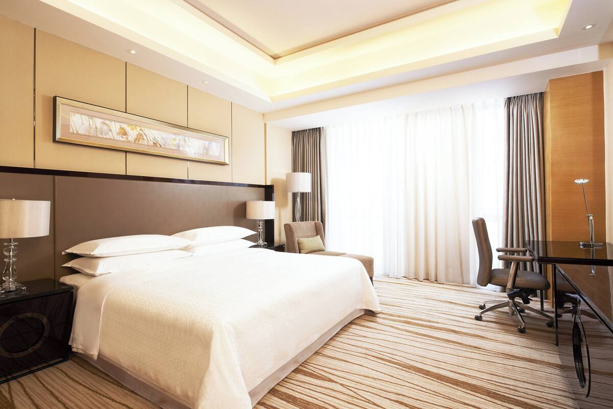 A hotel room with a large bed, a desk, a chair, and a lamp.