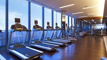 A gym with treadmills and elliptical machines, large windows, and exercise equipment.