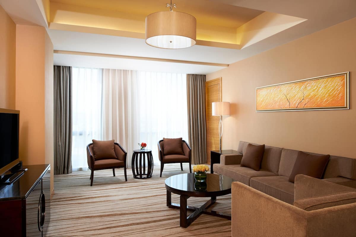 A hotel room with a large sofa, two armchairs, a coffee table, a TV, and a painting on the wall.
