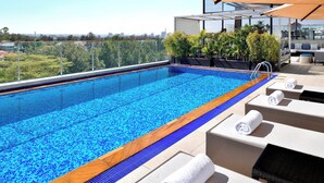 Une piscine à débordement située sur le toit, offrant une vue dégagée sur les toits de la ville, et entourée de chaises longues et d’un espace salon.