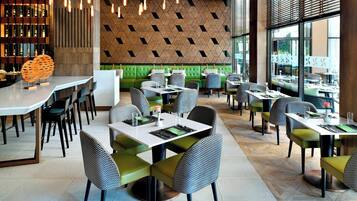 Un ristorante moderno con una parete a motivi geometrici, sedute imbottite verdi e diversi allestimenti tavola.