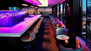 Un espace bar doté d’un long comptoir, de nombreux tabourets et offrant une vue sur la ville grâce à de grandes fenêtres.