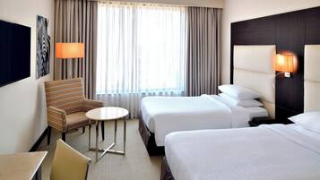 Ein Hotelzimmer mit zwei Betten, einem kleinen runden Tisch, einem Stuhl, einem Fernseher und einer Lampe.