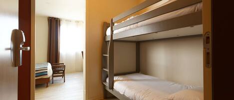 A bunk bed room with a wooden door, a small table, and a chair.